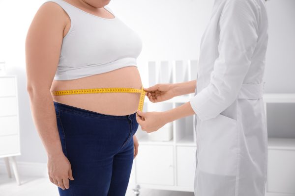 Doctor measuring waist of overweight woman in clinic, closeup